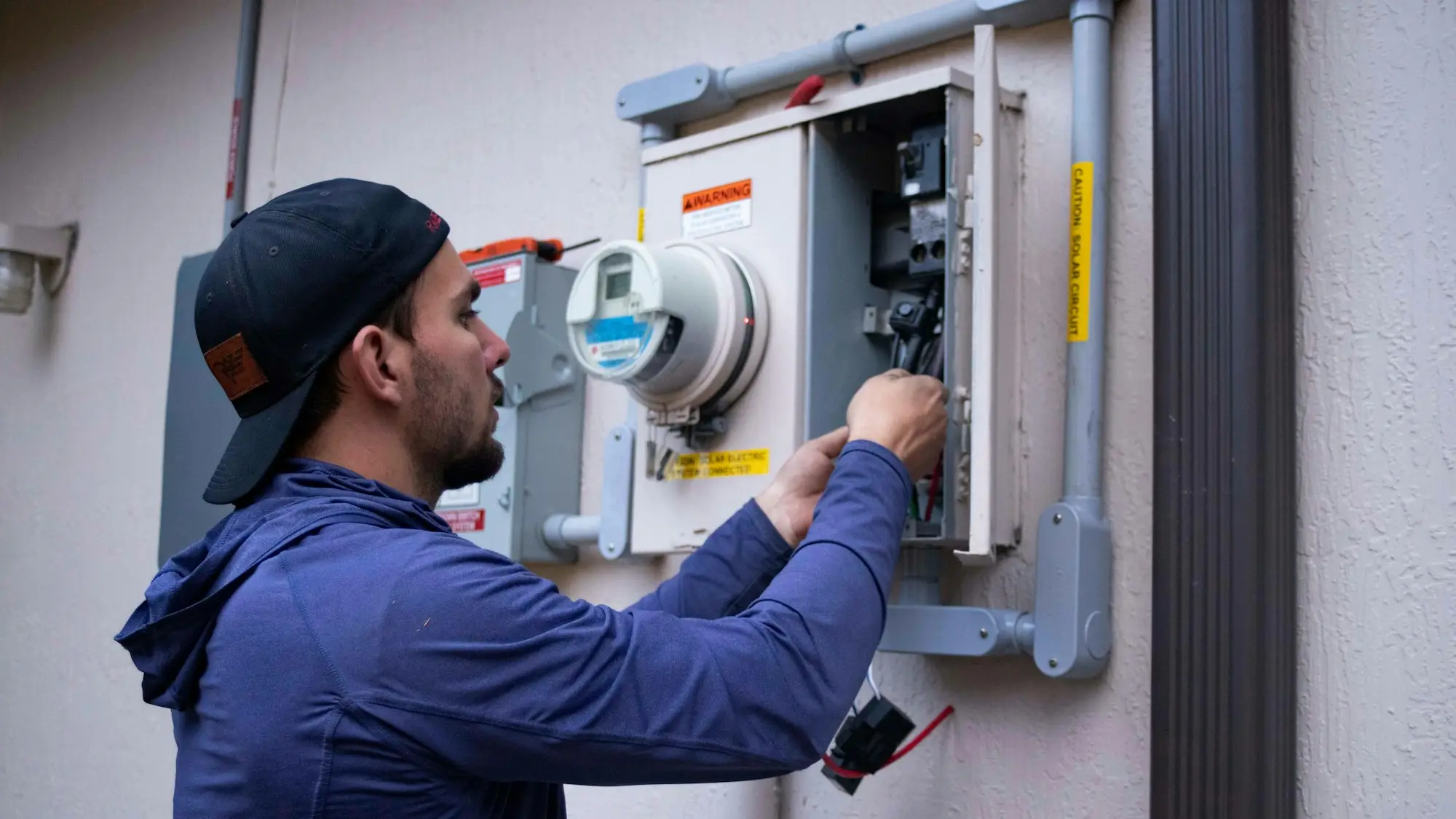 Electrician in a cap working on an electrical meter box