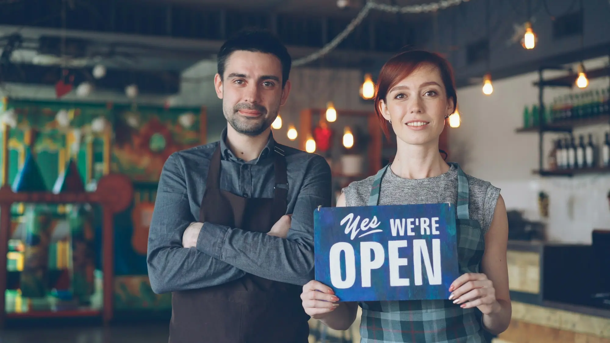 Two small business owners welcoming customers at the door with an open sign